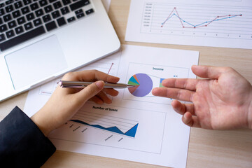 The hand of an Asian woman finance worker is pointing to a pie chart document to agree the work...