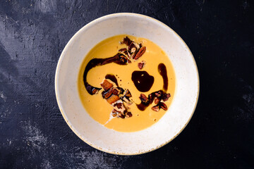 Black ceramic bowl of pumpkin cream soup with balsamic sauce, served pumpkin soup on a dark background