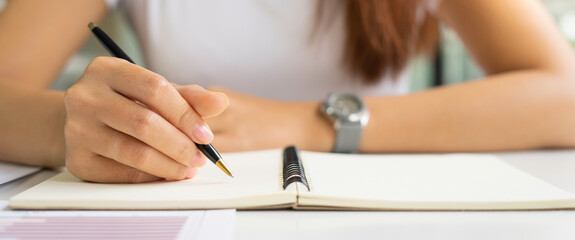 An Asian female is taking notes on her notebook for online classes, study ideas and note-taking.