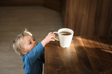 Little child try to grab cup of hot tea on the table. Attention hot content concept.