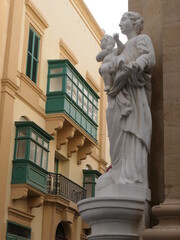 Valletta, Malta, December 25, 2020: A white statue of an angel on the corner of one of Valletta’s famous sandstone houses with colourful overhanging windows.