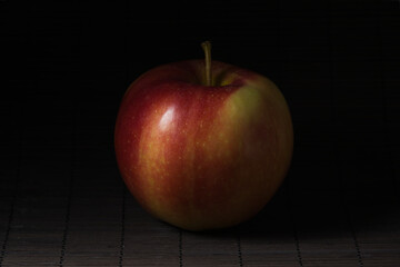 Subject photography: close-up of a ripe reddish-yellow apple on a dark straw mat.
