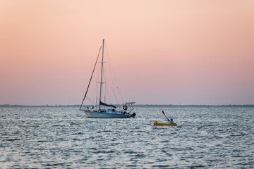 Fototapeta premium Distant view of man in the yellow colored boat near yacht that is in the sea