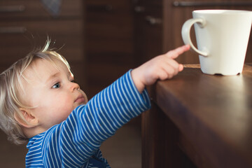 Little child try to grab cup of hot tea on the table. Attention hot content concept.
