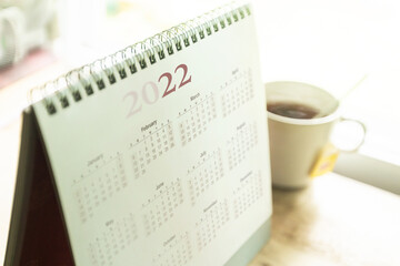 Paper desktop calendar 2022 schedule with tea cup on wooden desk	