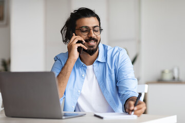 Young Arab Male Entrepreneur Talking On Cellphone And Taking Notes In Office