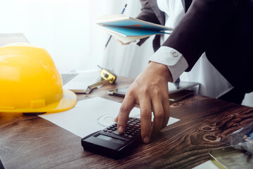 Two colleagues discussing data working and tablet, laptop with on on architectural project at construction site at desk in office