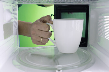 Young man heating food in the microwave. Green background for chroma key.