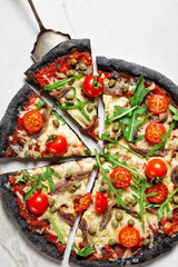 black dough pizza with anchovy arugula, capers