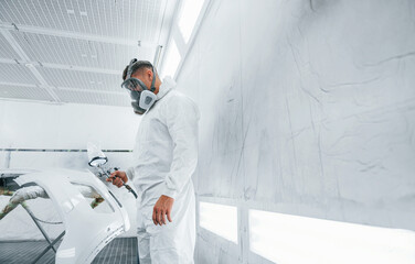 In protective mask. Painting the car. Caucasian automobile repairman in uniform works in garage
