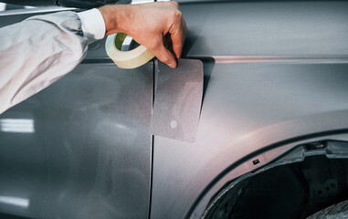 Applying new color. Caucasian automobile repairman in uniform works in garage