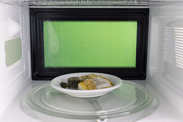 Young man heating food in the microwave. Green background for chroma key.