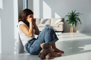 Young woman in casual clothes crying alone at home. Teddy bear lying down on the floor