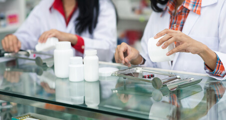 Two asian young woman pharmacist pour and count drug capsules on stainless tray, she prepare drug pack to patient in the pharmacy drugstore. Healthy and medicine concept.