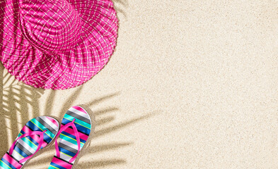 Fototapeta na wymiar Large round pink summer hat and colorful stripy sandals on sand with palm tree shadow