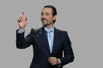 Smiling businessman using invisible interface. Handsome manager working on virtual screen against gray background.