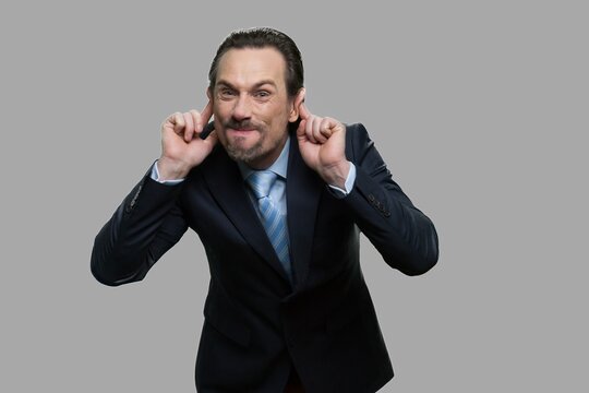 Mature businessman making monkey face. Caucasian man in business suit grimacing and teasing someone on gray background.