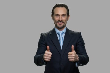 Handsome businessman showing two thumbs up. Attractive CEO looking at camera on gray background. Great success concept.