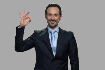 Handsome caucasian businessman gesturing ok with fingers. Man with happy facial expression looking at camera on gray background.