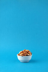 a bowl of peeled walnut isolated on blue background vertical image