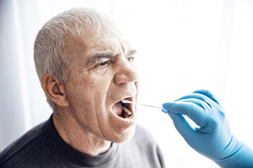 Medical worker wearing protective equipment testing senior old man for dangerous corona virus using test swab stick