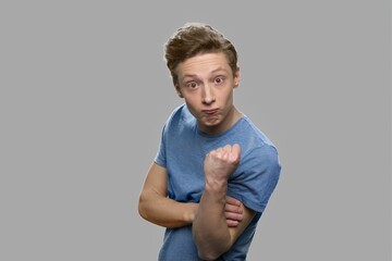 Irritated teen boy on gray background. Aggressive teenage guy threatens with fist. Human body...
