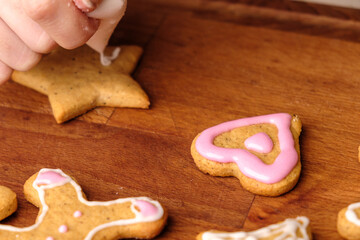 Fototapeta na wymiar Icing of Valentines Day. Woman decorating gingerbread cookies in the shape of heart on a wooden table.