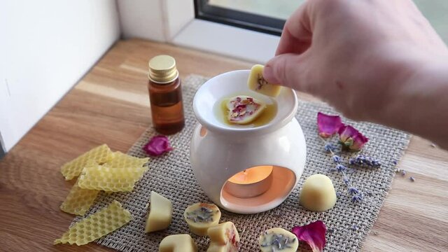 Using homemade mini wax melts in aromatherapy lamp diffuser at home interior concept. Melts making ingredients on table for unbleached beeswax, solid coconut oil, essential oil, dried flowers.