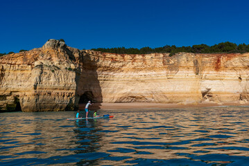 father and twho young children paddle on a SUP board along the Algarve coast in Portugal