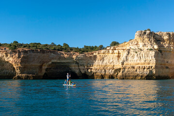 father and twho young children paddle on a SUP board along the Algarve coast in Portugal