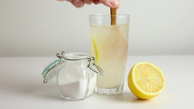Baking soda in drinking glass with water and lemon juice, health benefits for digestive system concept. Light background.