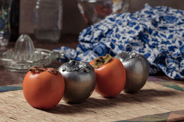 Silver and natural persimmons and kitchen tools, on a wooden table.