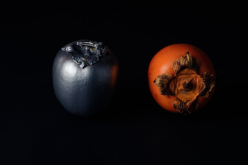 Artistic approach of natural and silver persimmons on a black background against light.