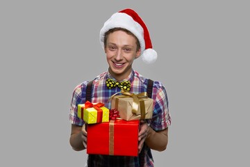 Cheerful teen guy in Santas hat offering gift boxes. Merry Christmas and happy New Year.