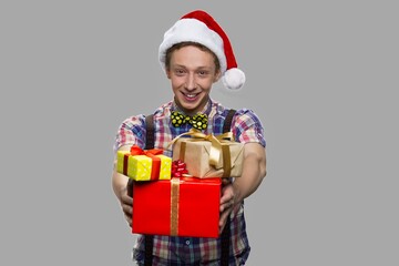 Funny teen guy handing Christmas gift boxes. Christmas teen boy with stack of gift boxes looking happy on gray background. Winter holiday celebration.