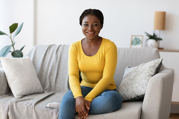 Beautiful Black Millennial Woman Sitting On Couch At Home, Smiling At Camera