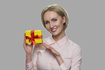 Close up happy smiling woman showing gift box. Attractive business lady holding small gift box on gray background.