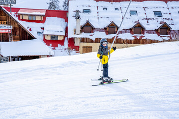 Auron, France 31.12.2020 A boy lifting on the ski drag lift rope in bright sport outfit over sun...