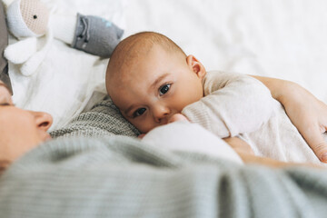 Young mom with cute baby boy, mother breast feeds baby on the bed, natural tones