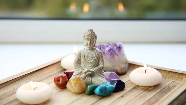 All seven chakra colors crystals stones around sitting Buddha figurine on natural wooden tray. Balance and calm energy flow in home concept.