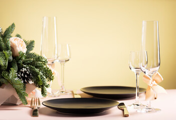 Table setting for a festive dinner for two, black plate and glasses with flower arrangement on yellow background, side view, copy space, horizontal orientation