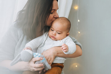 Young mother playing with cute baby boy in bright bedroom, natural tones, love emotion
