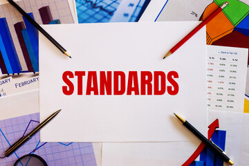 The word STANDARDS is written on a white background near colored graphs, pens and pencils. Business...