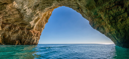 panorama view from inside a cave on the ocean coast with turquoise water and sunny blue sky outside