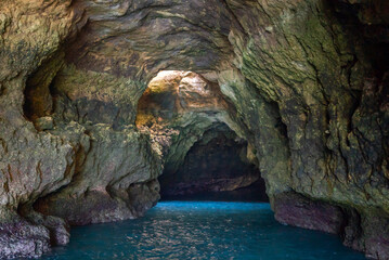 view from inside a cave on the ocean coast with turquoise water and sunny blue sky outside