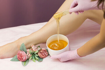 Obraz na płótnie Canvas Hair removal in a luxury spa studio. Women's feet wax with saccharin. Hot sugar. The product of the wax bowl. Salon bank. Purple, lilac background
