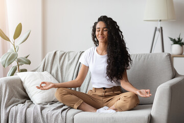 Peaceful brunette lady sitting on couch, meditating