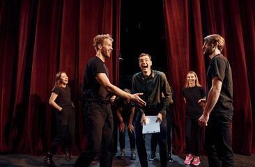 Working together. Group of actors in dark colored clothes on rehearsal in the theater - obrazy, fototapety, plakaty
