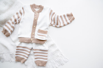 New white and light brown, warm sweater with trousers on light gray table background. Baby clothes for winter time. Flat lay. Top down view.