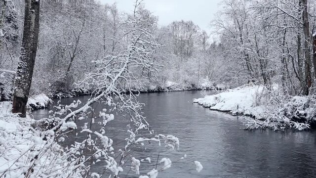 Long shutter speed photo of river water flowing in winter nature, surrounded by trees covered by fresh snow. Keila river in Estonia.